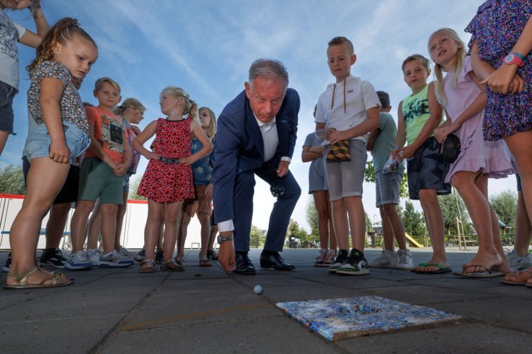 Wethouder plaatst knikkertegel van gerecycled pmd bij basisschool CNS de Groenling in IJsselmuiden